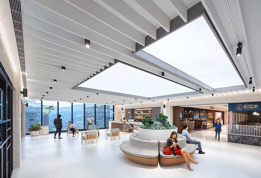 A group of people sitting in a large room with a large glass ceiling.